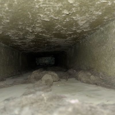 View inside a dusty air duct showing accumulated debris and dirt.