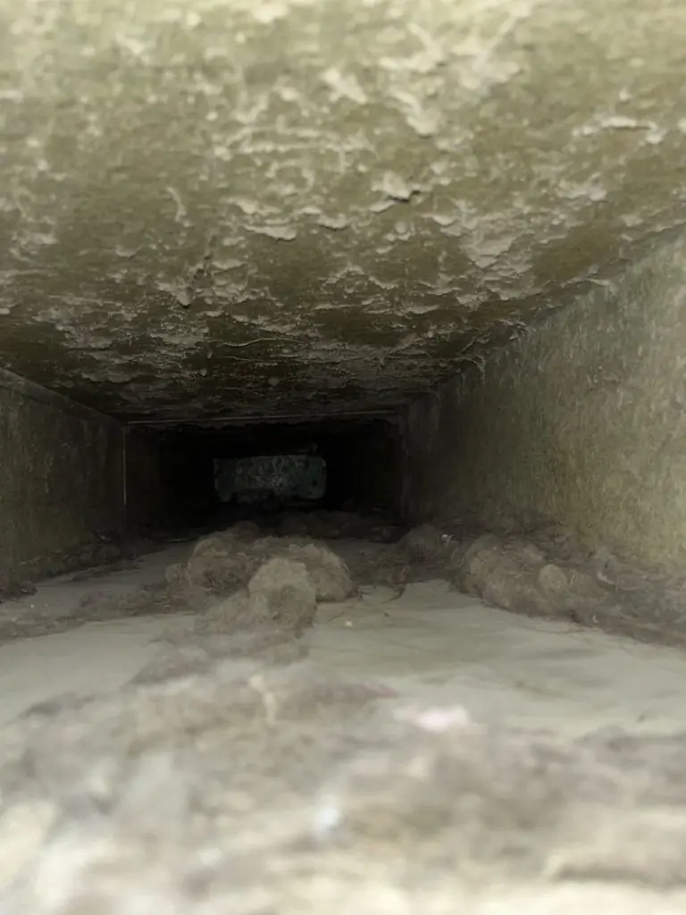 View inside a dusty air duct showing accumulated debris and dirt.