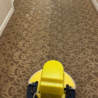 Yellow carpet cleaning machine in a hallway with patterned carpet and an open door on the left side.