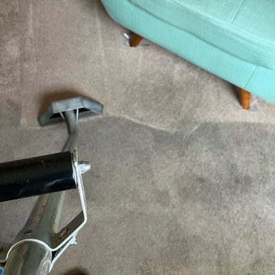 Carpet cleaning tool in use on a beige carpet with visible clean and dirty sections, next to a light green chair.