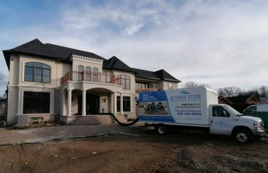 Rivers Edge Carpet & Duct Cleaning truck parked in front of a large two-story house with a hose extending inside for duct cleaning.