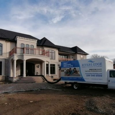 Rivers Edge Carpet & Duct Cleaning truck parked in front of a large two-story house with a hose extending inside for duct cleaning.